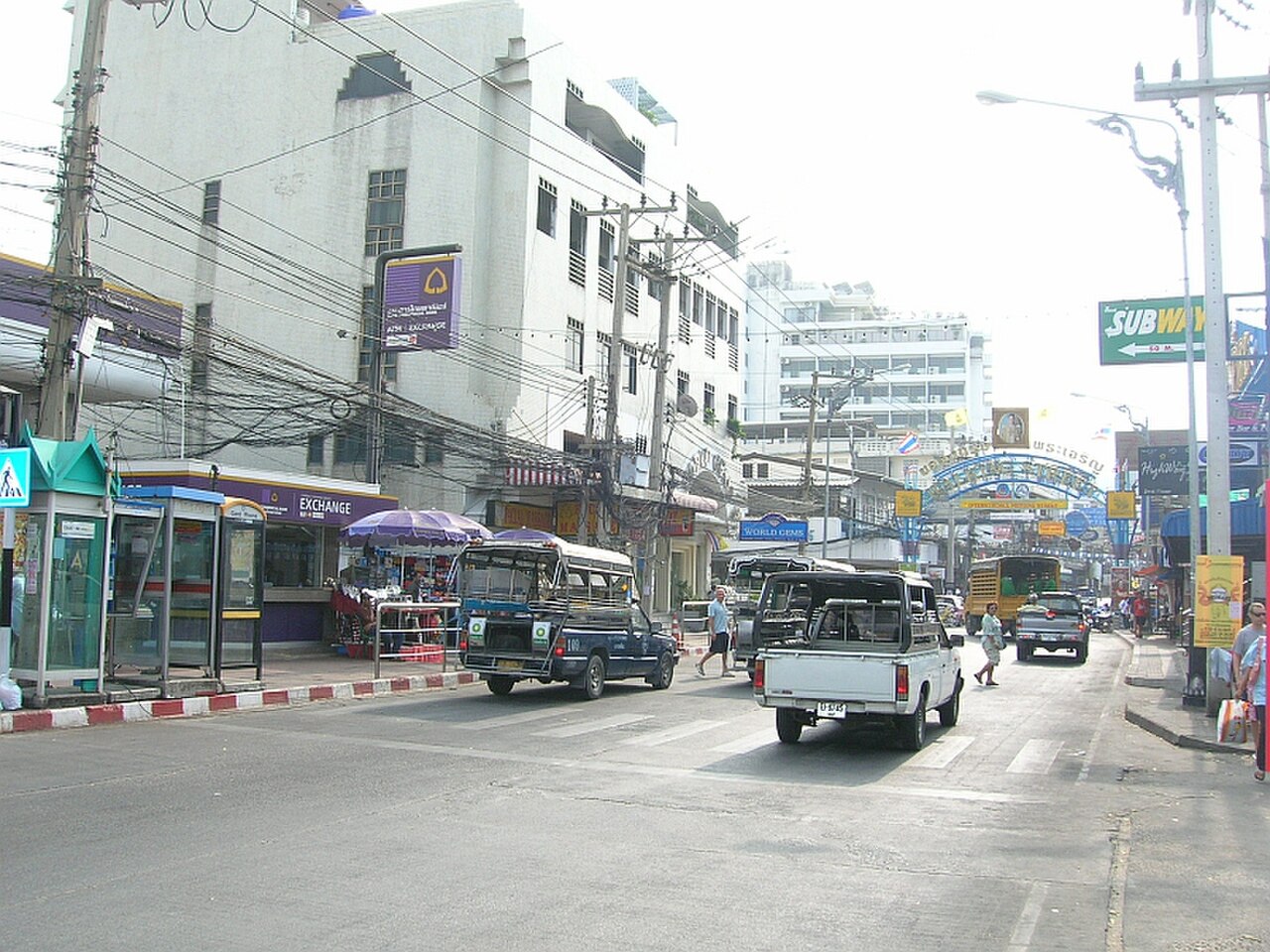 The entrance to Pattaya Walking Street in daytime — the entrance arch in the distance, blue baht-bus songthaews on the beachfront road