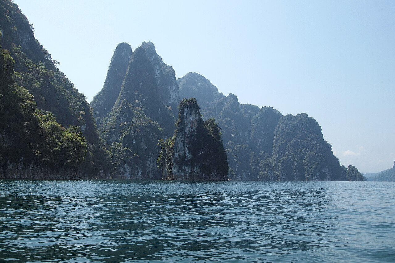 ทะเลสาบเชี่ยวหลานในอุทยานแห่งชาติเขาสก — เขาหินปูนปกคลุมป่าฝนเขียวชอุ่มโผล่ขึ้นจากผิวน้ำสีเขียวมรกตนิ่งสงบ