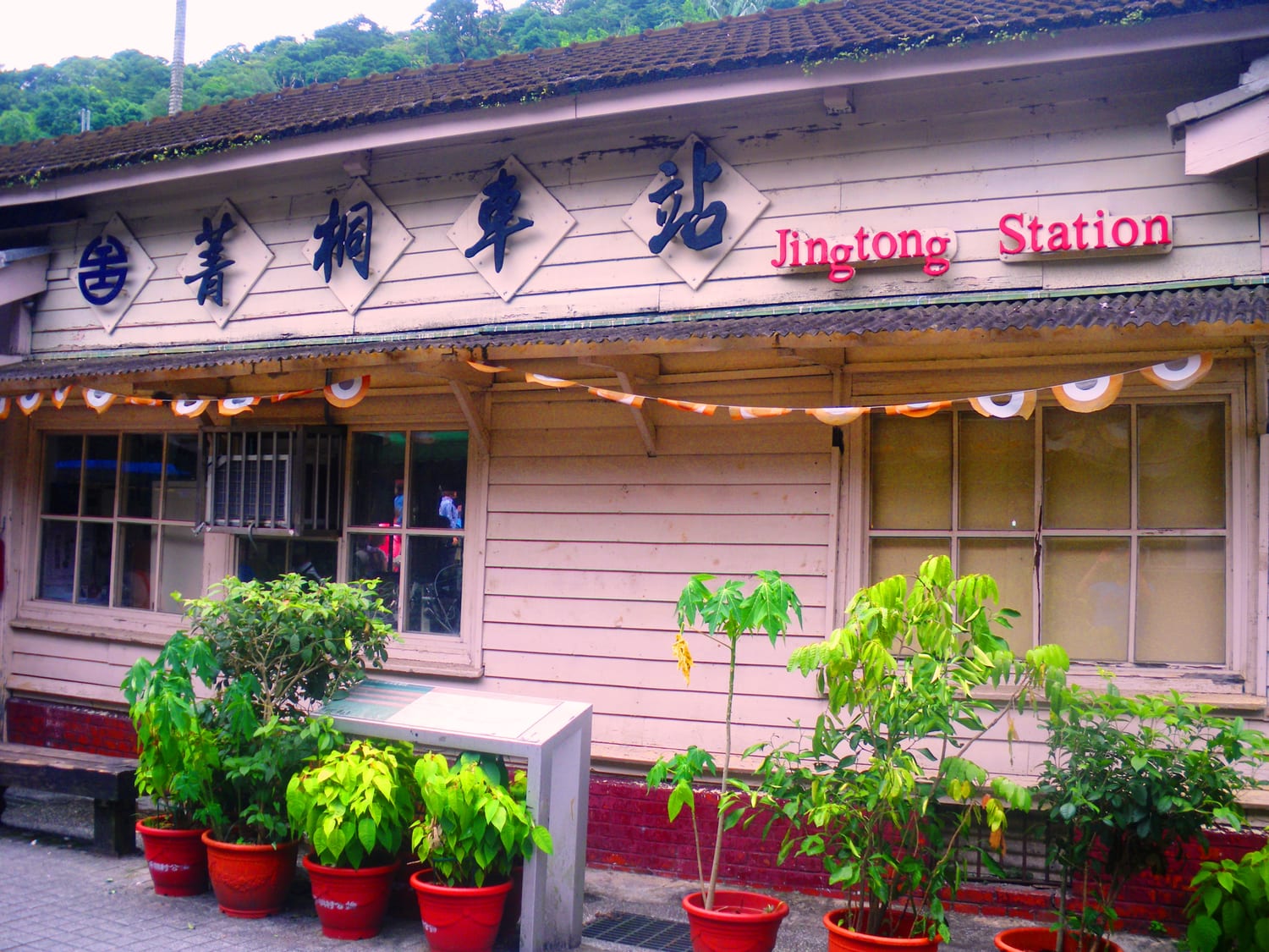 สถานีรถไฟจิ้งถงไม้เก่าสมัยอาณานิคมญี่ปุ่นบนรถไฟสายผิงซี มีกระถางต้นไม้สีแดงเรียงหน้าสถานี