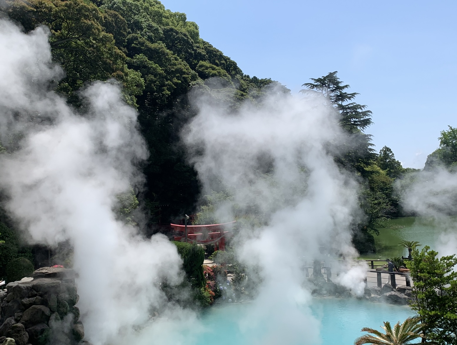 Umi Jigoku (บ่อนรกทะเล) เบปปุ — บ่อน้ำร้อนสีน้ำเงินอมเขียว ควันพวยพุ่ง สะพานสีแดง ต้นไม้เขียว