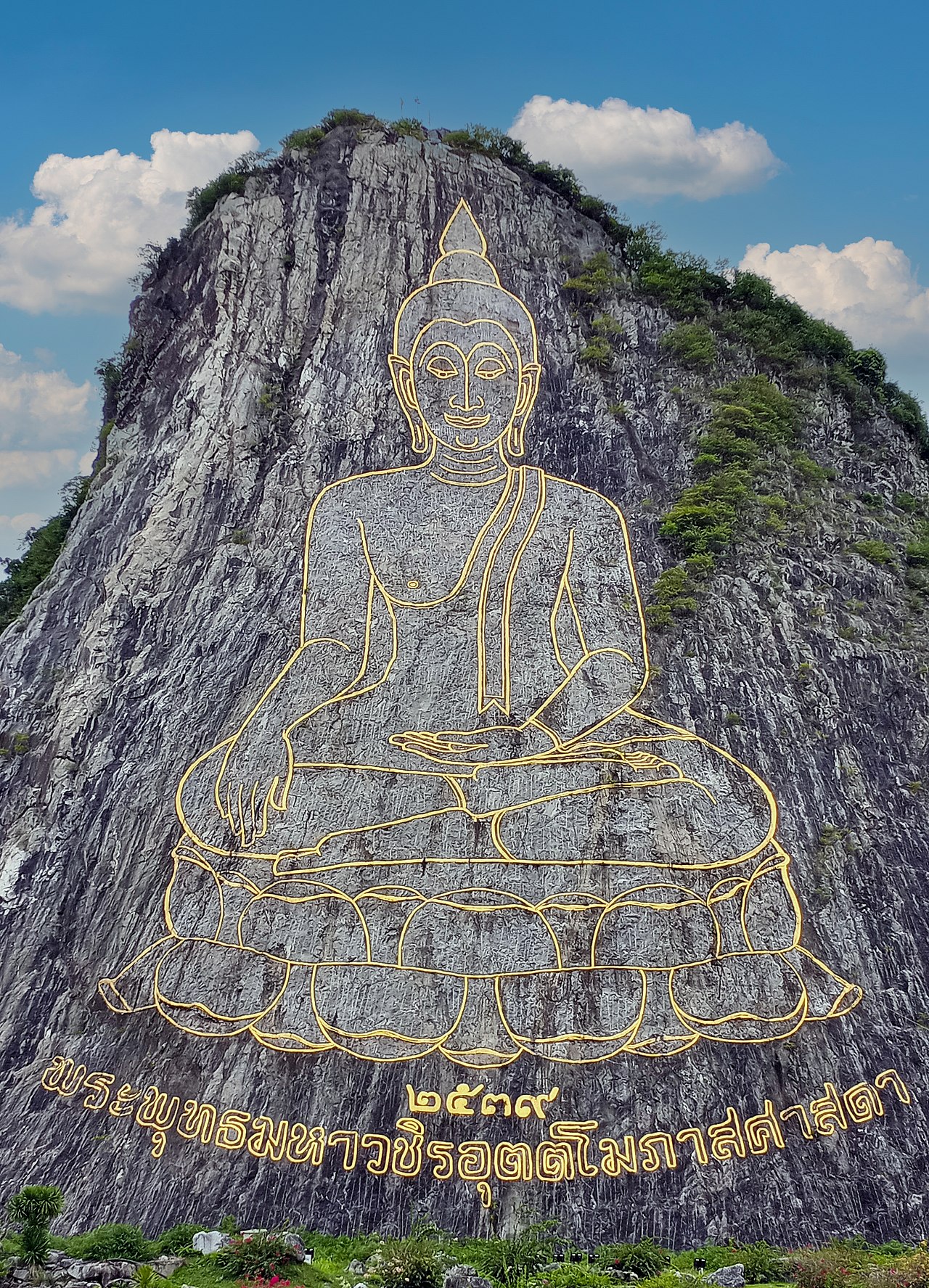 เขาชีจรรย์ พัทยา — พระพุทธรูปปางสมาธิสลักเส้นทองบนหน้าผาหินสูง ใหญ่ที่สุดในโลก ท้องฟ้าสีฟ้าและต้นไม้รอบเขา