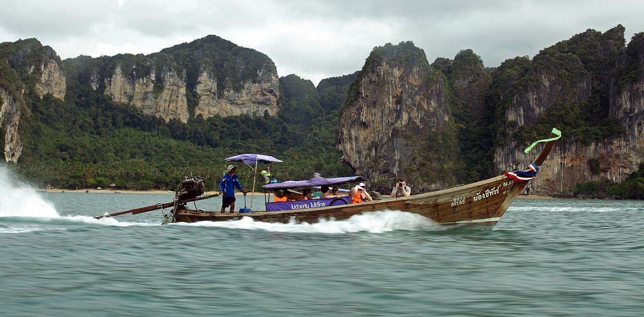 เรือหางยาวบรรทุกนักท่องเที่ยวแล่นข้ามทะเลกระบี่ มีหน้าผาหินปูนเป็นฉากหลัง — การเดินทางไปไร่เลย์