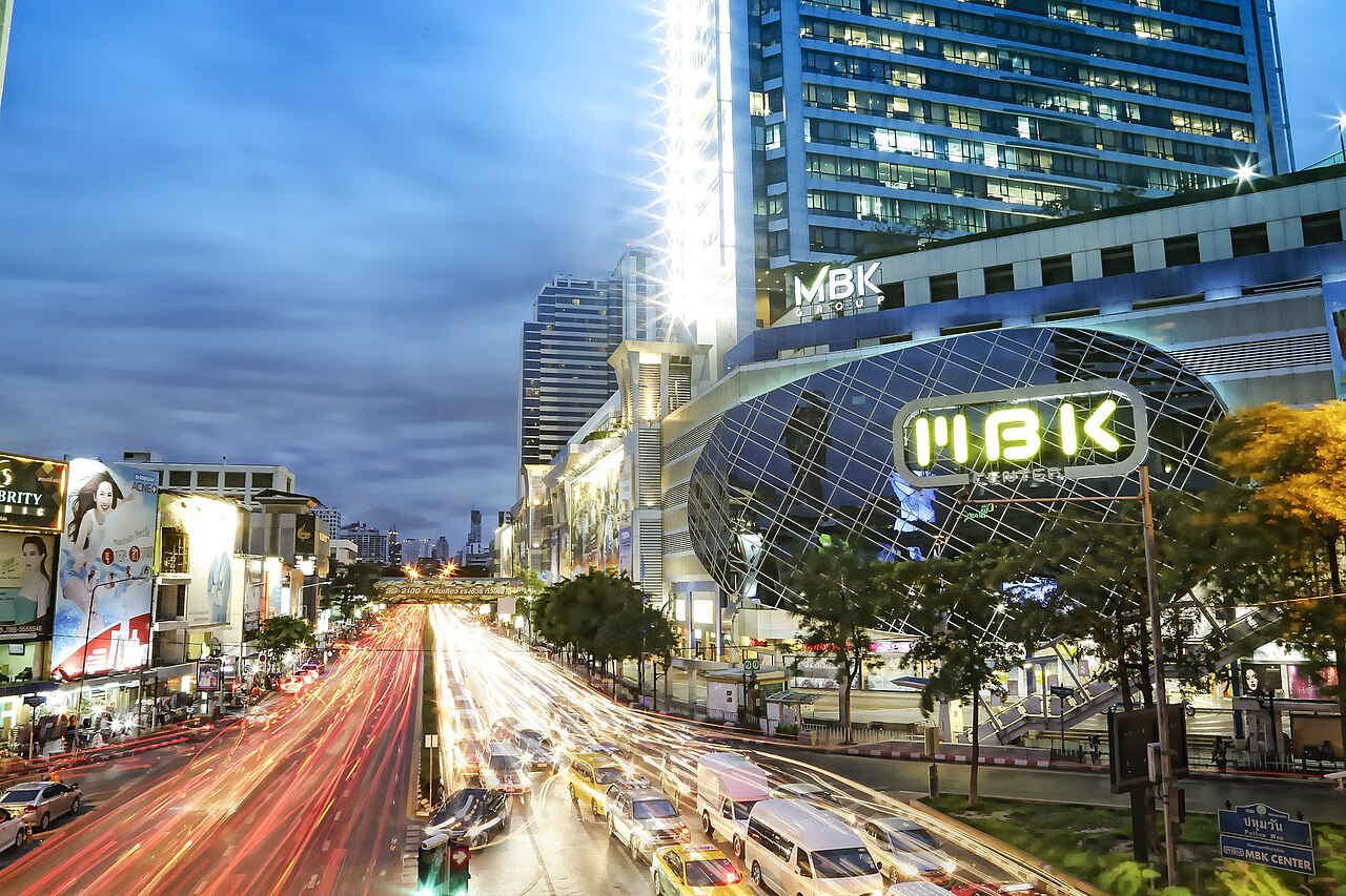 ห้าง MBK Center หัวมุมแยกปทุมวันยามค่ำ ไฟรถวิ่งเป็นเส้นยาวบนถนนพญาไท ภายในห้างมีฟู้ดคอร์ท MBK Food Island ชั้น 6