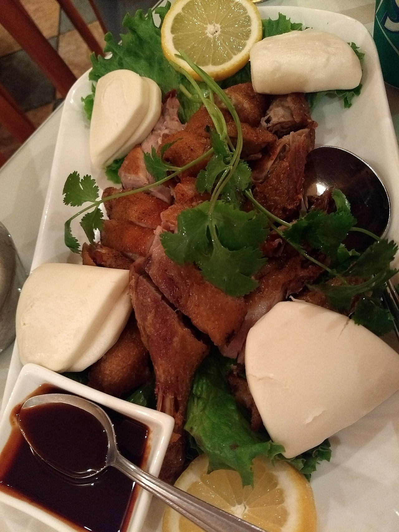 Zhangcha duck — crisp golden-brown sliced tea-smoked duck served with steamed buns, lemon and lettuce on a white platter