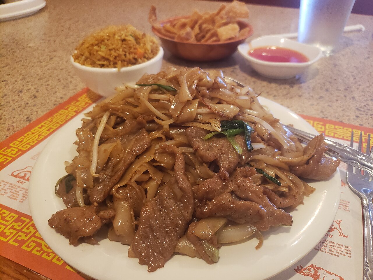 Dry-fried beef ho fun — wide flat rice noodles seared with beef strips and bean sprouts on a blue-and-white plate, with a light char from the wok