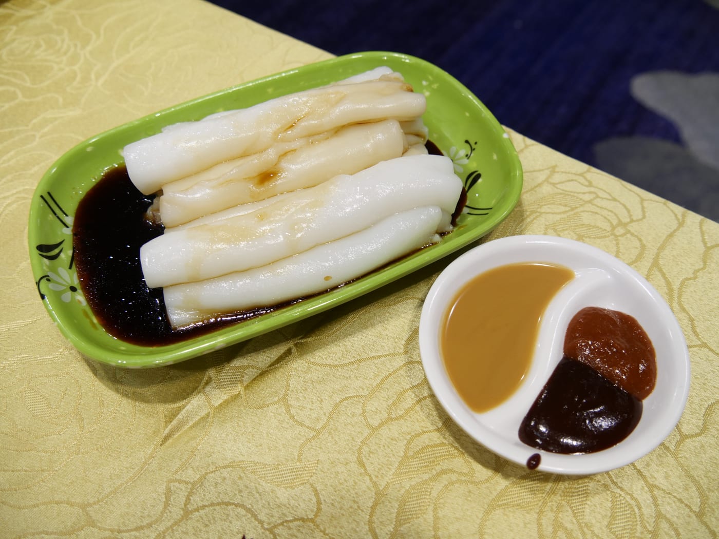 Cheung fun — silky white steamed rice-noodle rolls in dark sweet soy sauce, served with sesame and hoisin dipping sauces