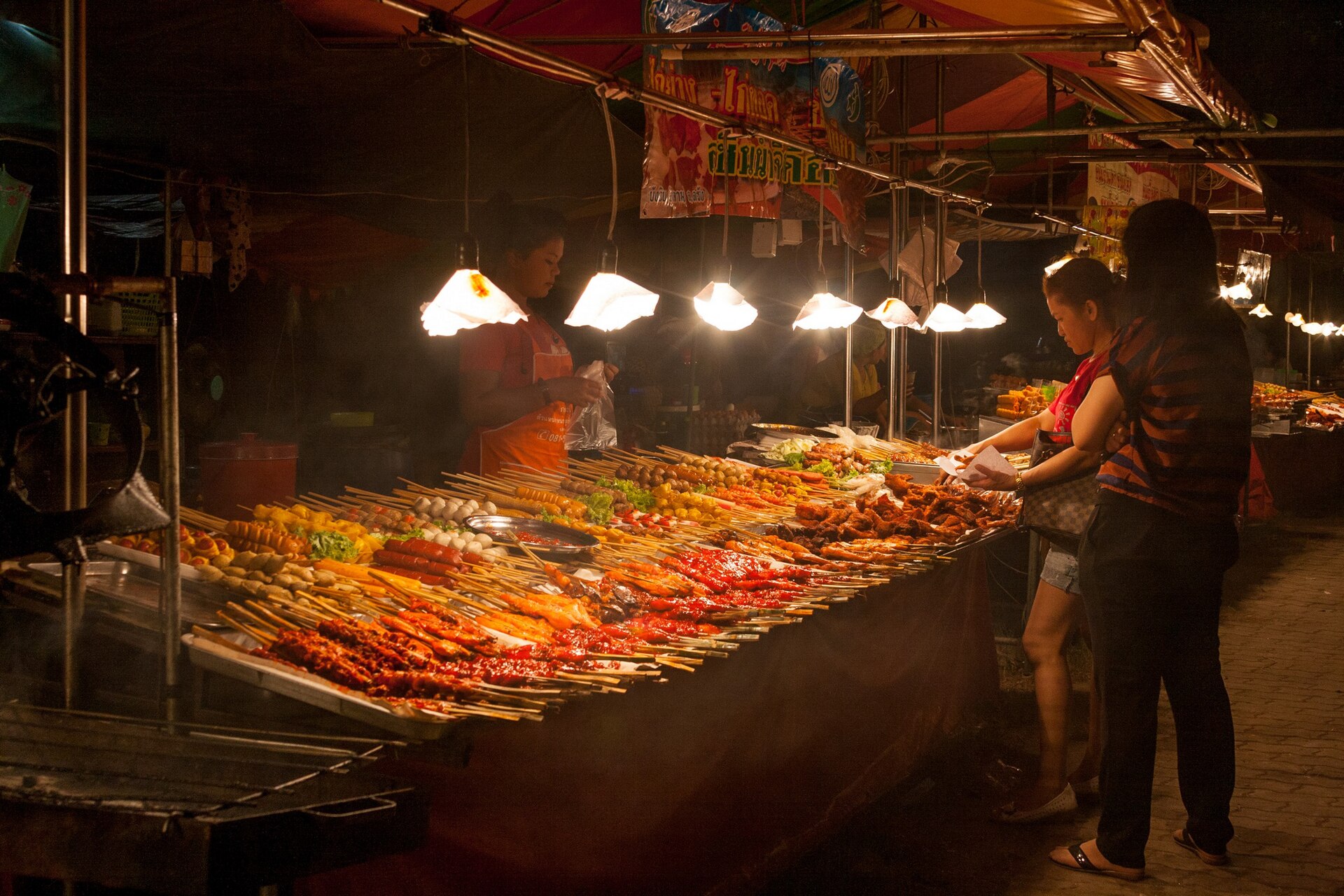 แผงปิ้งย่างที่ตลาดกลางคืนกระบี่ กับซีฟู้ดและของเสียบไม้เรียงราย ไฟส่องสว่าง — แหล่งกินยามค่ำราคาถูก