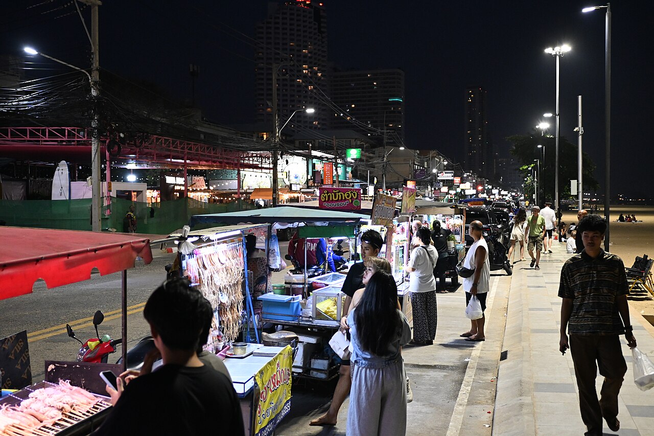 รถเข็นสตรีทฟู้ดเรียงรายเลียบทางเดินริมหาดจอมเทียนพัทยายามค่ำ มีทะเลและตึกสูงเป็นฉากหลัง
