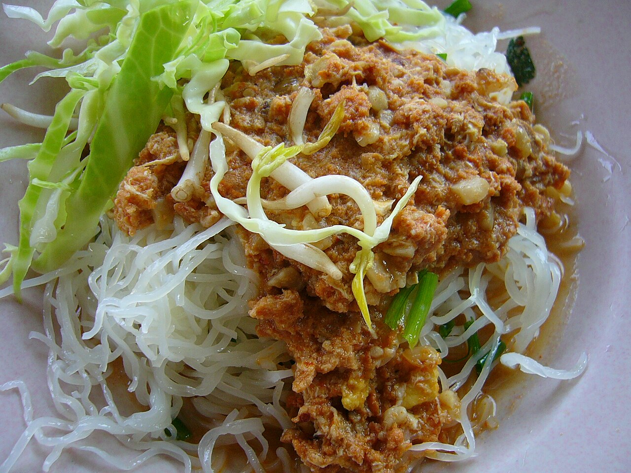 ขนมจีนภูเก็ต เส้นขนมจีนราดน้ำยาปลา โรยผักกะหล่ำและถั่วงอก กินกับผักเหนาะ