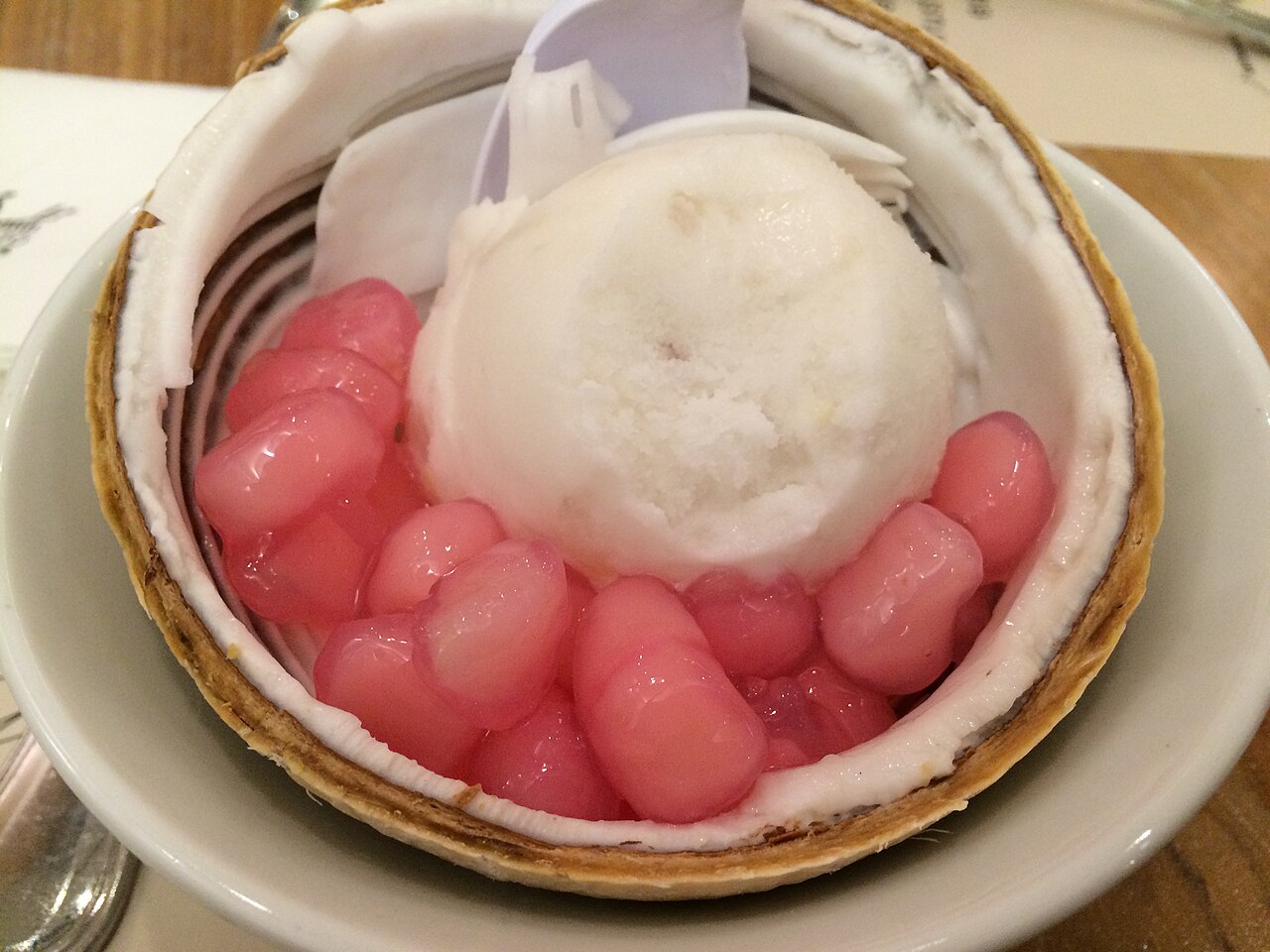 ไอศกรีมมะพร้าวเสิร์ฟในลูกมะพร้าวอ่อนผ่าครึ่ง โปะทับทิมกรอบสีชมพู