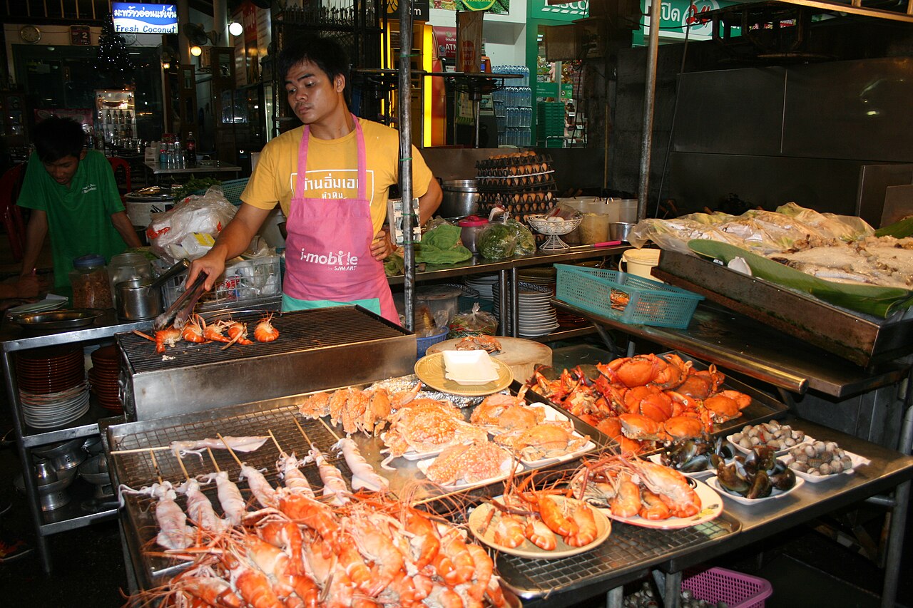 แผงซีฟู้ดย่างยามค่ำสไตล์ตลาดไทย กุ้งเผา ปูนึ่ง และหมึกเสียบไม้เรียงเต็มหน้าร้าน