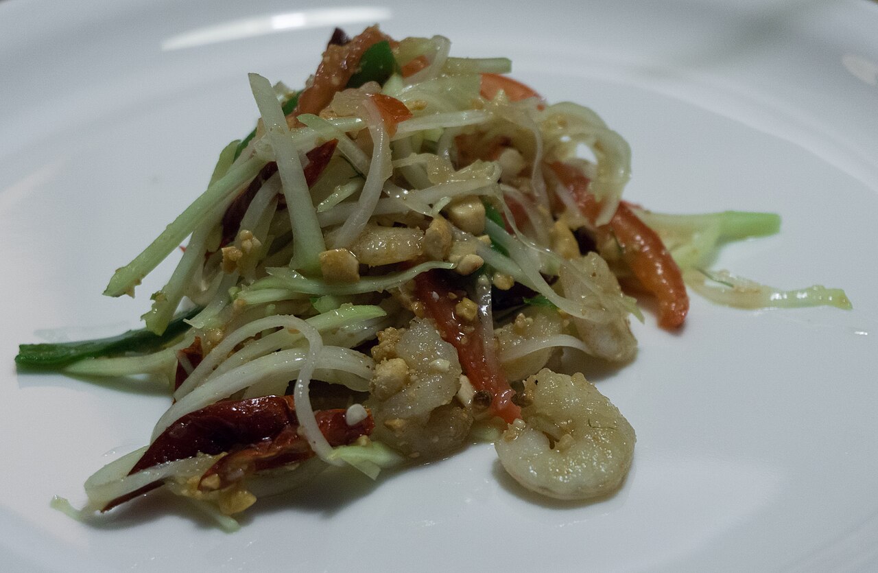 ส้มตำไทยใส่กุ้งสด มะเขือเทศ พริกแห้ง และถั่วลิสง จัดมาในจานขาว