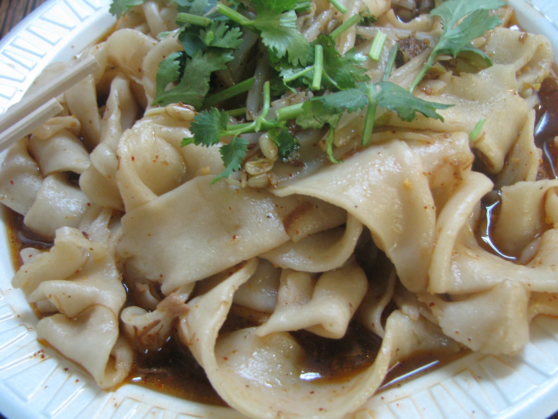 บะหมี่เบี่ยงเบี่ยงซีอาน — เส้นบะหมี่แบนกว้างหนาในชามโรยพริกป่นแดง ต้นหอม ราดน้ำมันร้อน