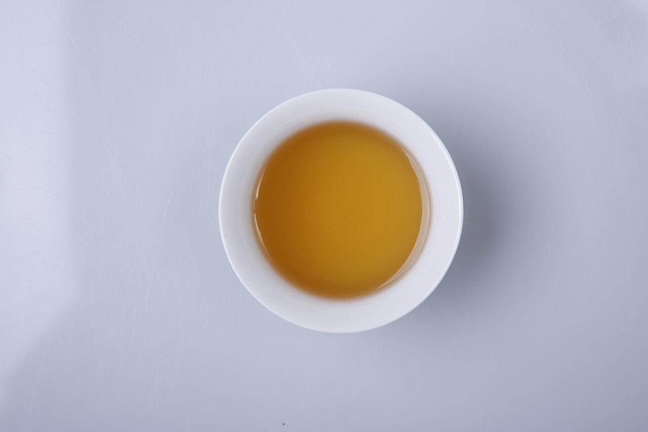 Zhangjiajie vine tea (莓茶) brewed into a clear amber-gold liquor in a white cup — the city's signature herbal tea, faintly bitter then sweet on the throat