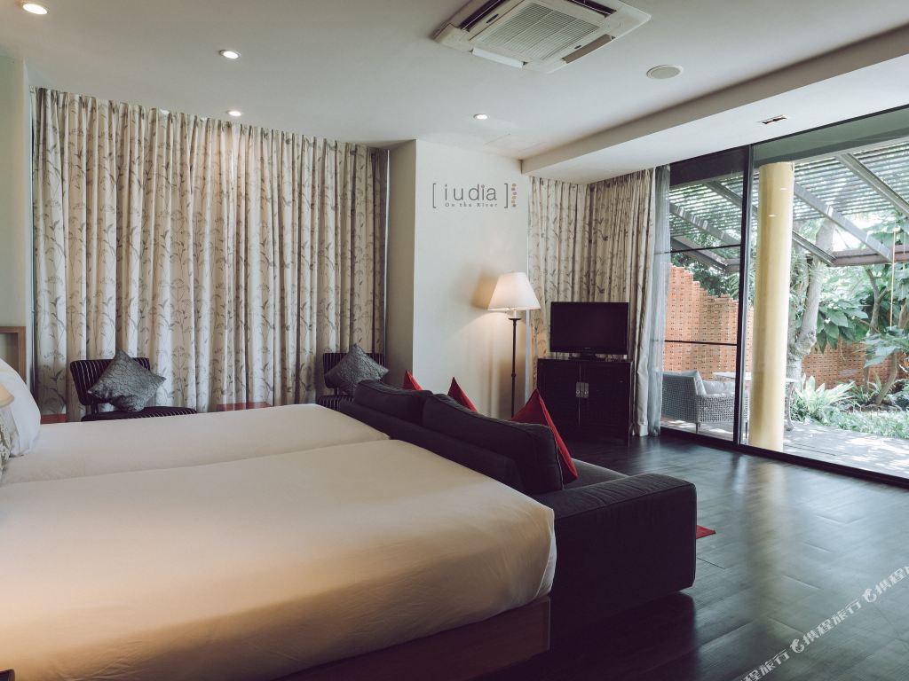 ห้องพักกว้างพื้นไม้สีเข้ม ผนังมีโลโก้ iuDia เปิดสู่ระเบียงสวน
