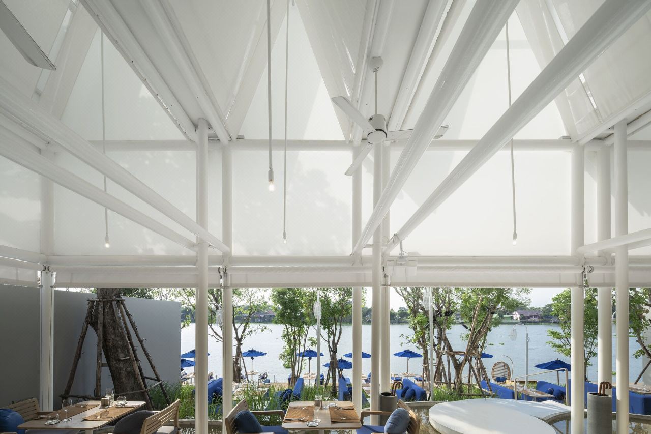 Canvas-roofed riverside restaurant on the Chao Phraya bank with blue poolside umbrellas
