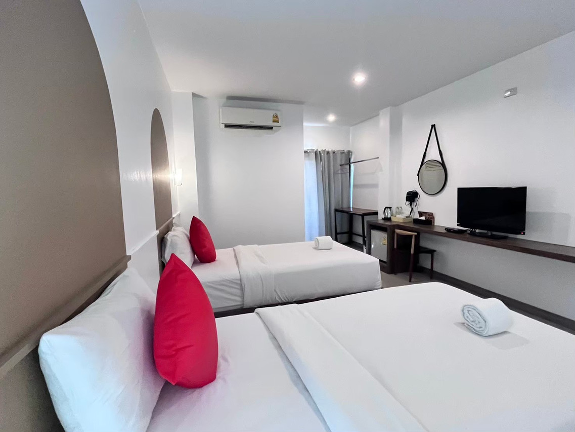 ห้องพักเตียงคู่โทนขาวพร้อมหมอนอิงสีแดงและโต๊ะทำงานของ The S Design Hotel