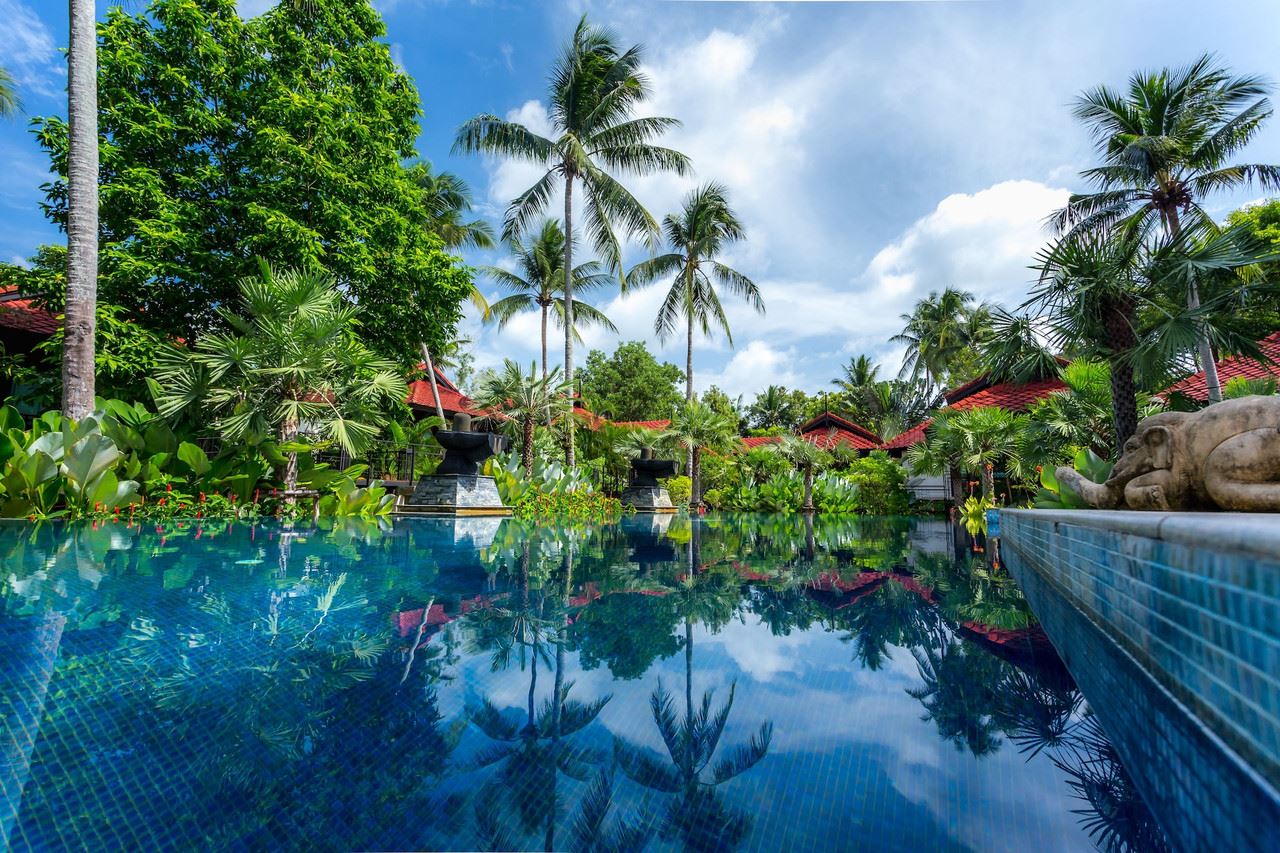 สระว่ายน้ำเกลือในโซนสวนของ Tusita Wellness Resort ล้อมด้วยวิลล่าหลังคากระเบื้องและต้นมะพร้าว