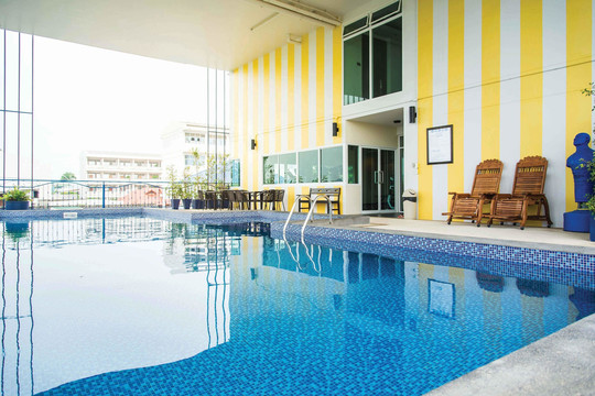 Indoor saltwater pool at The Bridge Residence Hotel with yellow-and-white striped wall, wooden loungers and a poolside seating area