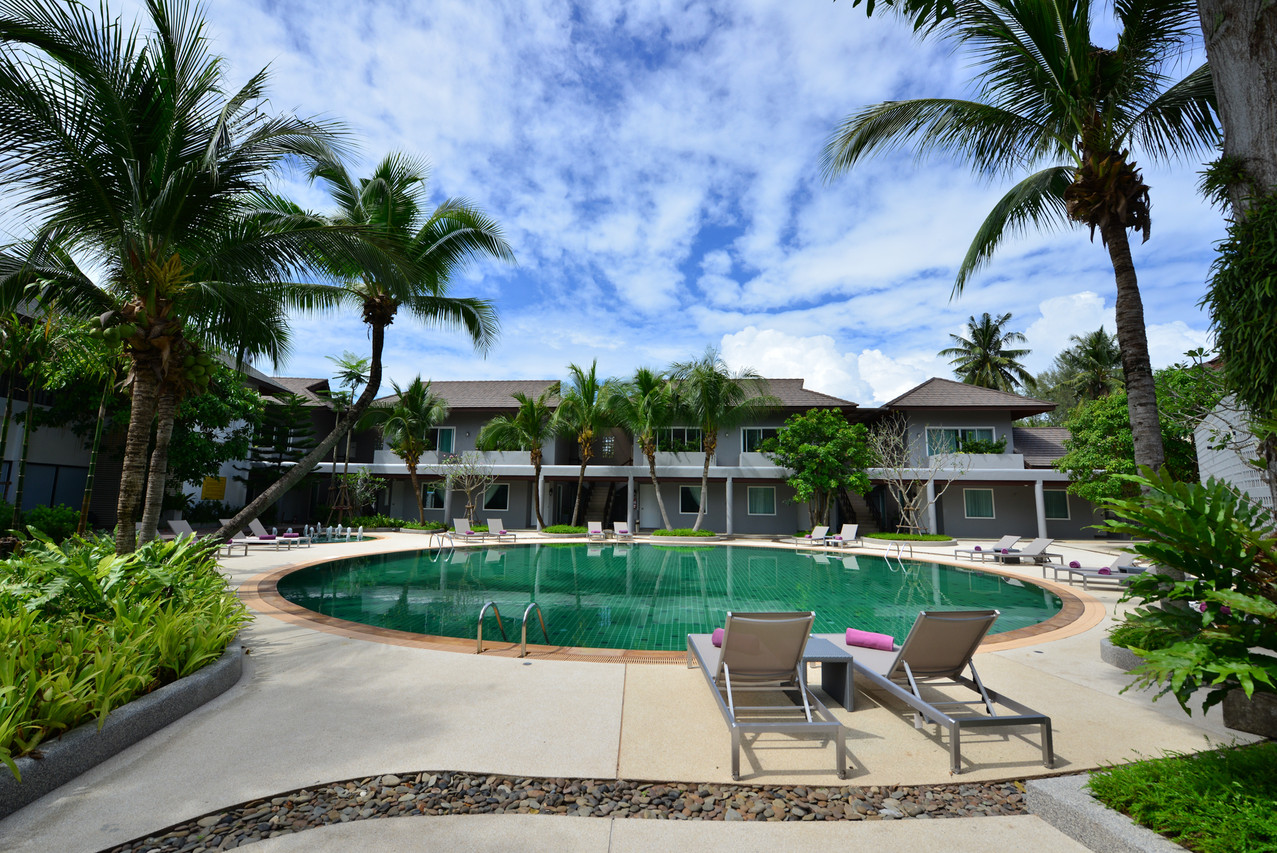 Garden swimming pool with dark grey villa buildings among coconut palms