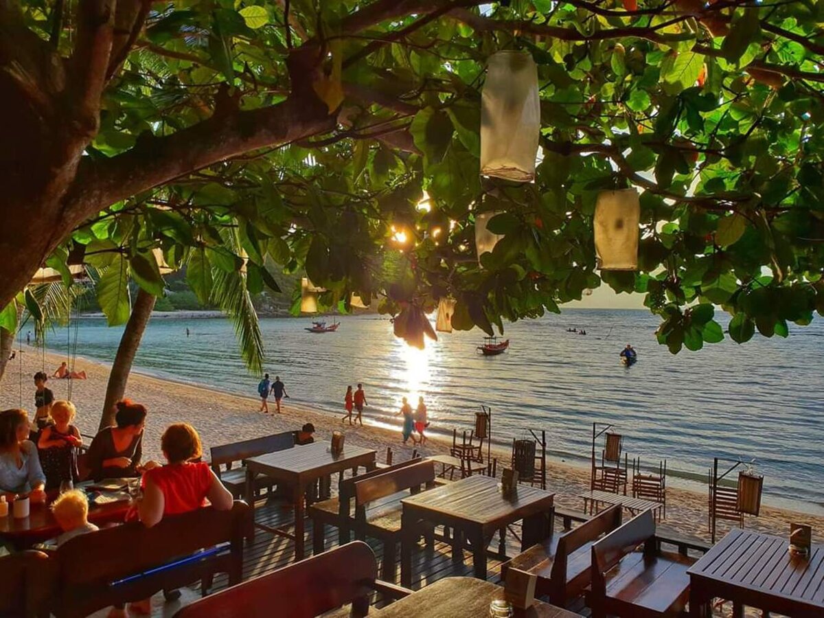 Beachfront restaurant under a shade tree with evening lanterns over Haad Salad bay
