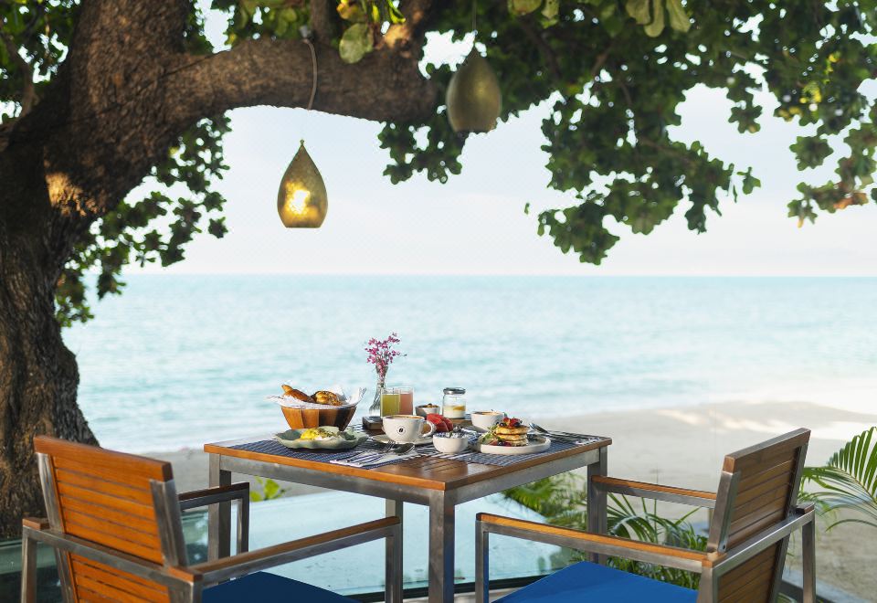 Beachfront dining table under a large tree facing the Gulf of Thailand at sunset
