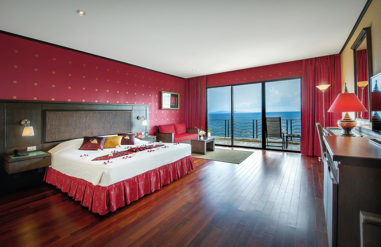Deluxe Suite with red walls and floor-to-ceiling glass opening to a cliff-edge balcony