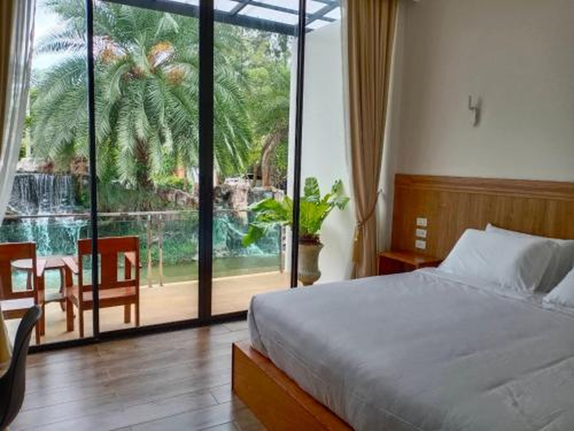 ห้องเตียงคิงเปิดกระจกบานใหญ่มองเห็นน้ำตกจำลองและต้นปาล์มที่ The Grand Jamjuree Resort ลำพูน