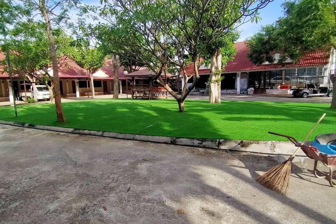 ลานสวนหญ้าเขียวมีต้นไม้ใหญ่ให้ร่มเงา ล้อมด้วยห้องพักหลังคากระเบื้องแดงของ Bansuan Resort
