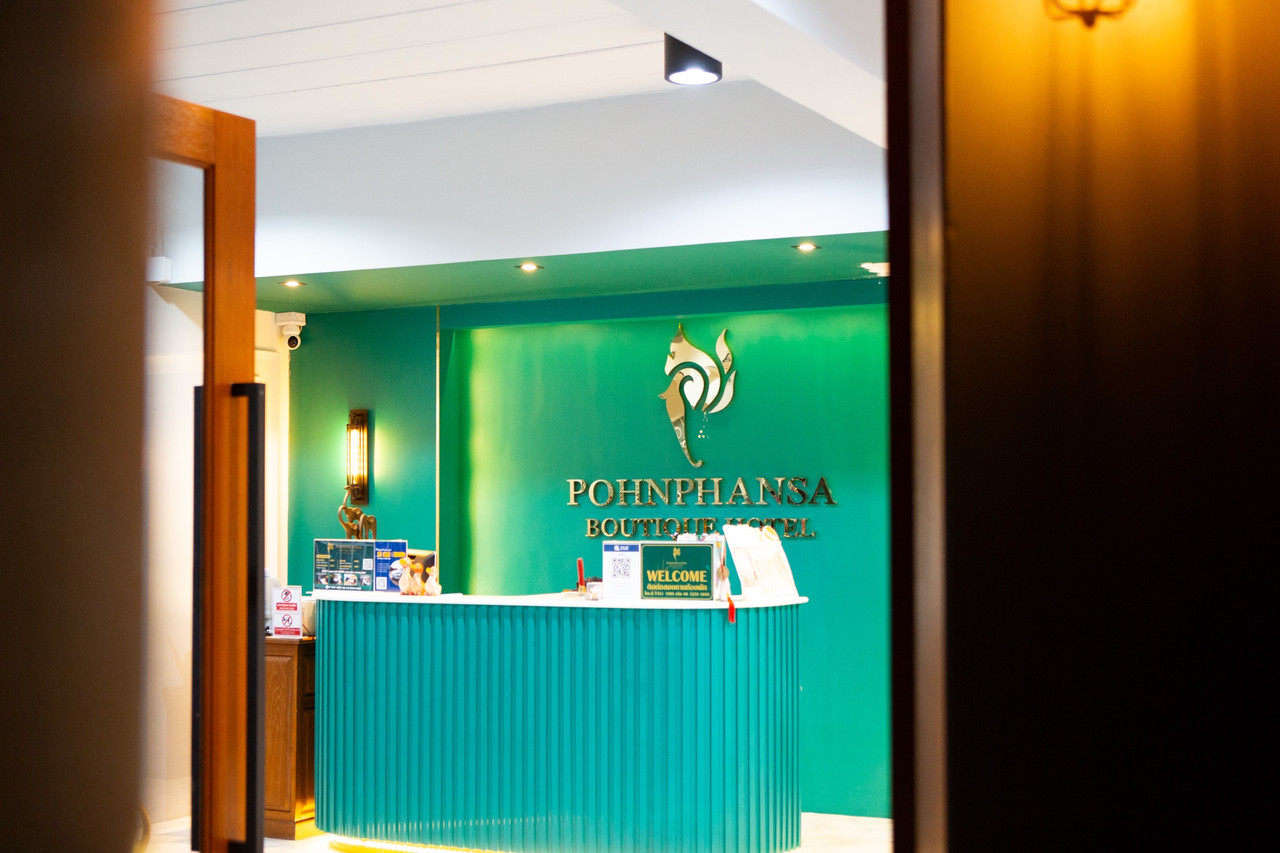 เคาน์เตอร์ต้อนรับสีเขียวมรกตกับโลโก้นกยูงสีทองและป้าย Pohnphansa Boutique Hotel