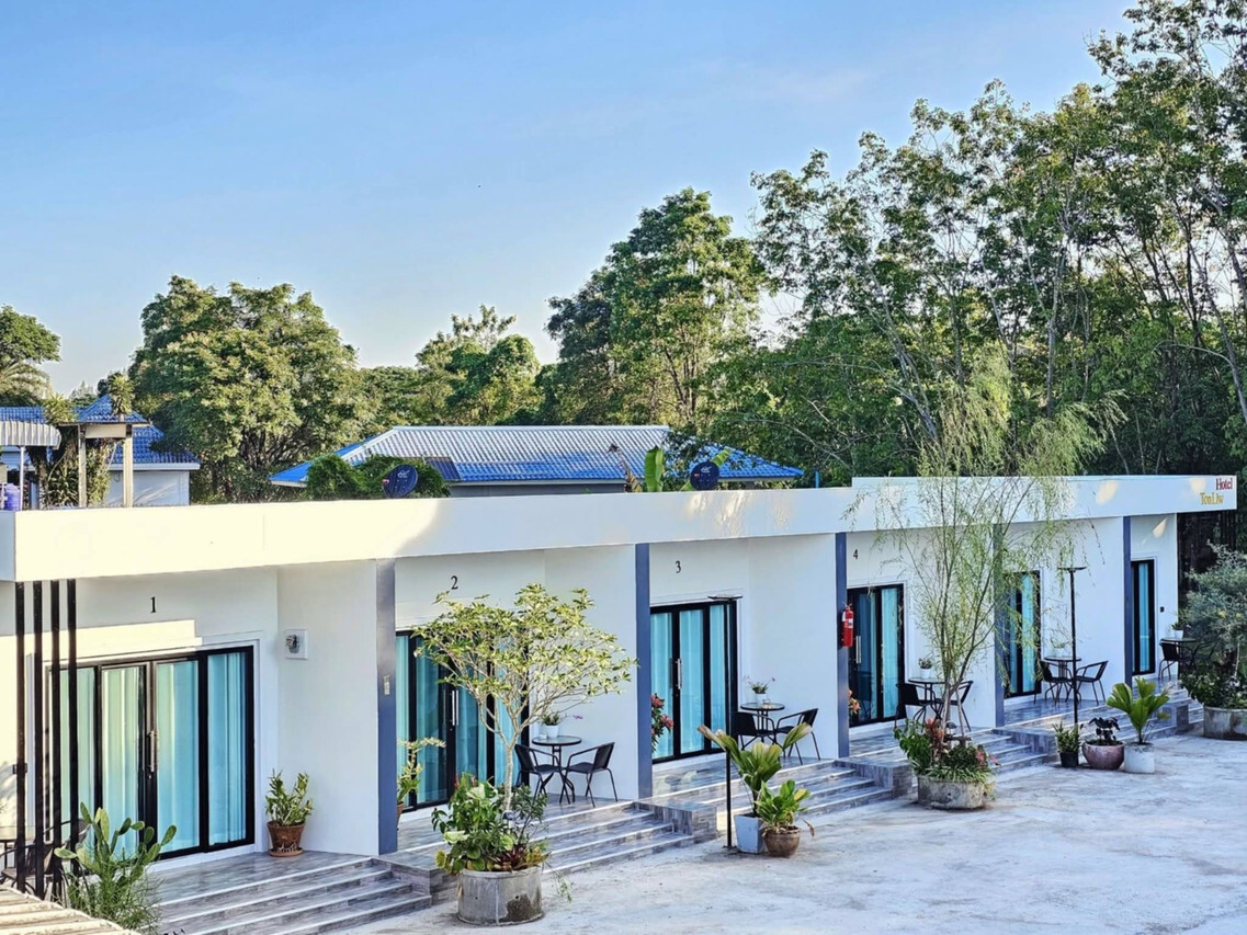 อาคารห้องพักชั้นเดียวสีขาวของ TonLiw Hotel มองจากด้านข้างพร้อมสวนต้นไม้