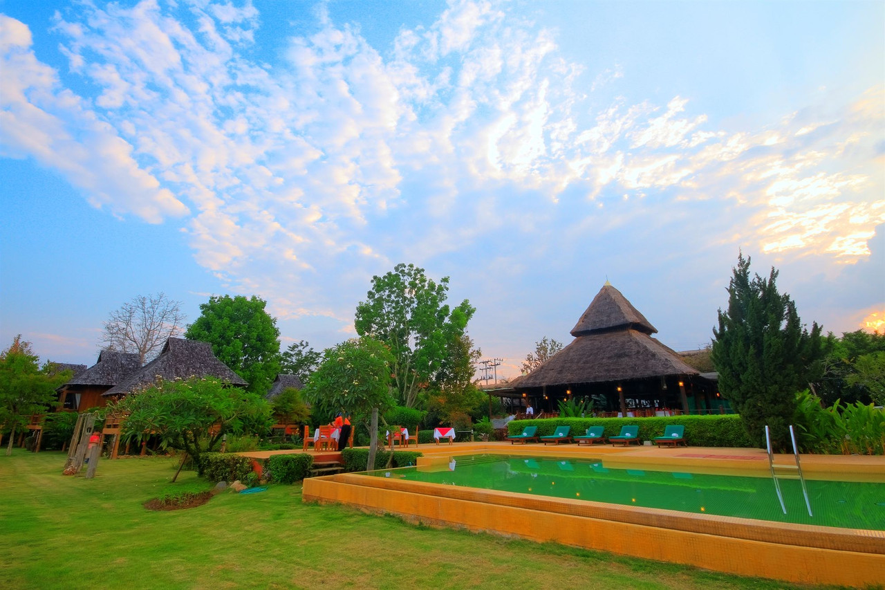 สระว่ายน้ำกลางแจ้งกับศาลาร้านอาหารหลังคามุงจาก Belle Villa Resort Pai ช่วงเย็น