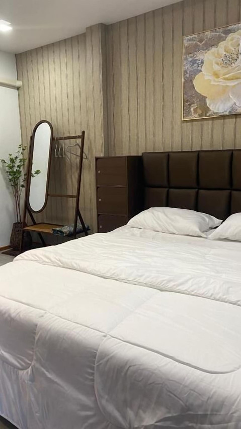 ห้องนอนเตียงใหญ่ผ้าปูสีขาว ผนังลายไม้ พร้อมกระจกเงาตั้งพื้น
