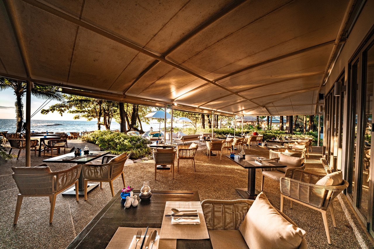 Beachfront restaurant with pebble flooring, rattan chairs and an evening sea view