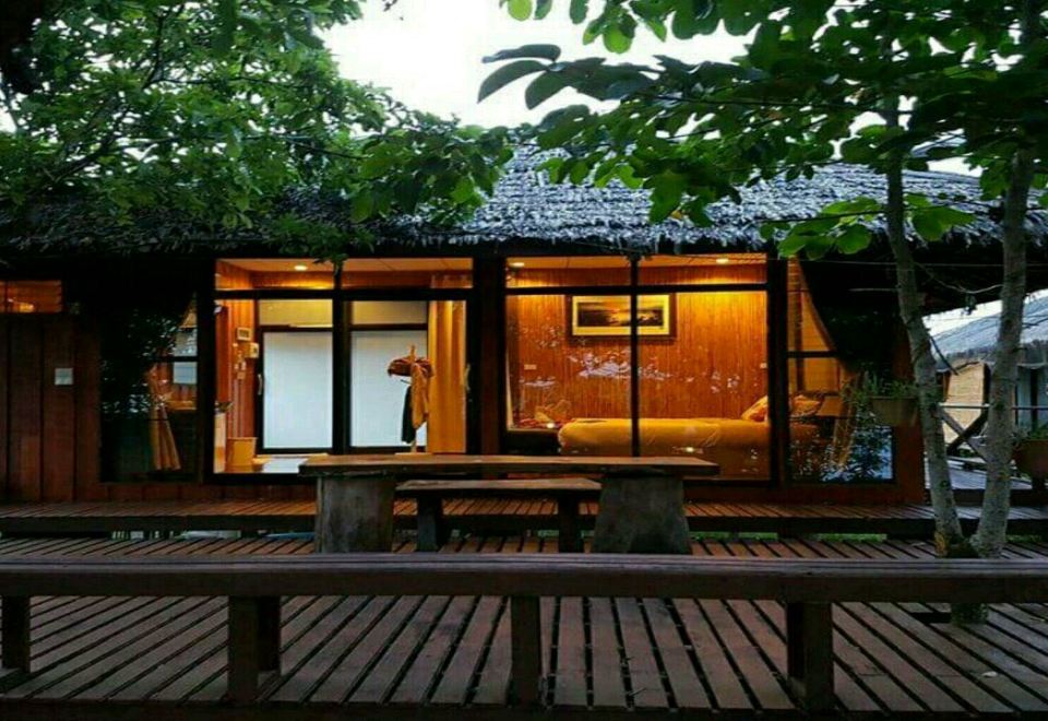 บ้านไม้หลังคาจากพร้อมระเบียงไม้ของ Rimlay Park Resort ยามเย็น