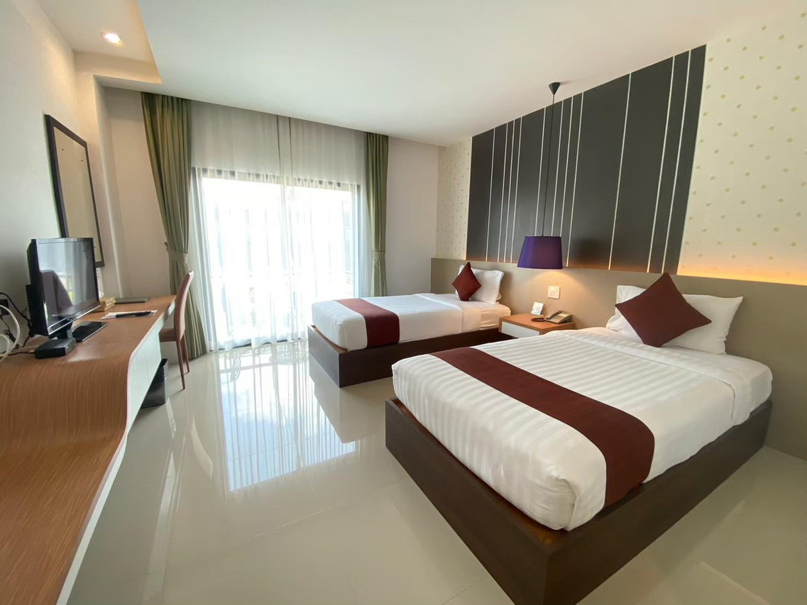 ห้อง Deluxe ของ Siva Royal Hotel เตียงคู่ ผนังลายเส้นสีเข้ม พื้นมันวาว มีโต๊ะทำงานและระเบียง