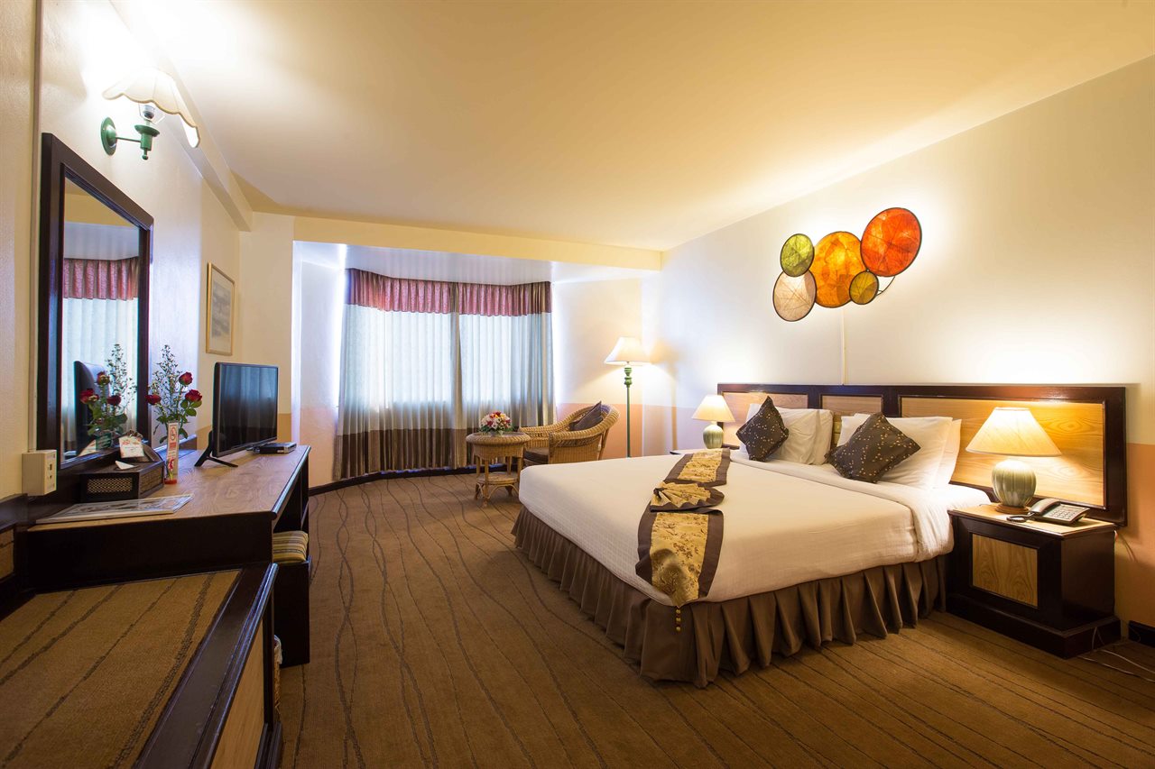 ห้องพักโทนไม้สีอุ่นของ Phayao Gateway Hotel เตียงใหญ่ปูผ้าขาวคาดผ้าลายไทยและงานศิลป์เปลือกหอยบนผนัง