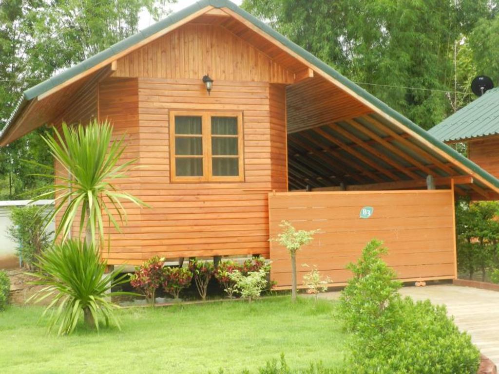 บ้านไม้สักหลังเดี่ยวหลังคาเขียวพร้อมสวนหญ้าและไม้ประดับหน้าเรือน