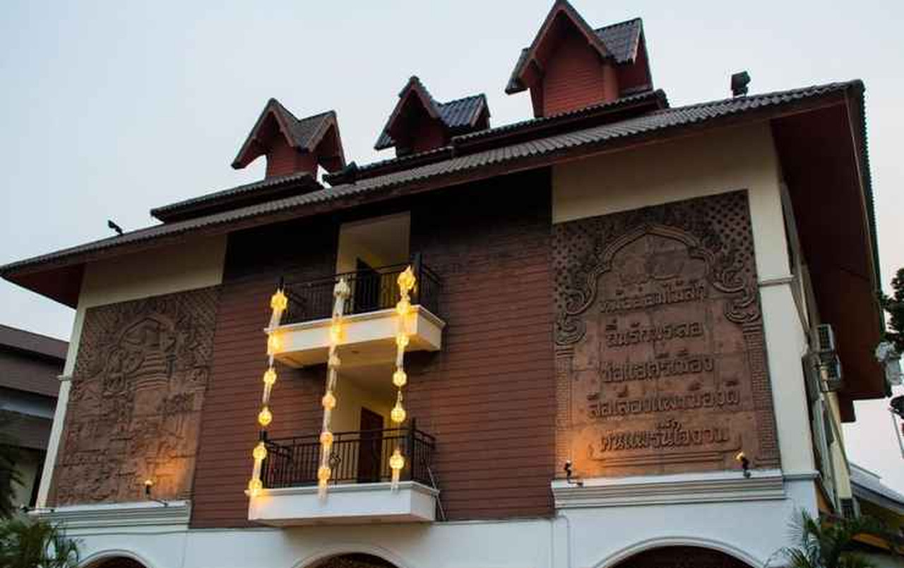 ผนังไม้สักแกะสลักลายล้านนาด้านหน้าอาคารพร้อมระเบียงประดับโคมไฟ