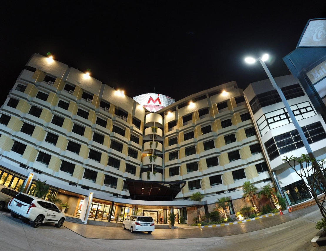 อาคาร M Grand Hotel Roi Et ยามค่ำ ป้ายตัว M สว่างกลางตึกโค้ง กลางเมืองร้อยเอ็ด
