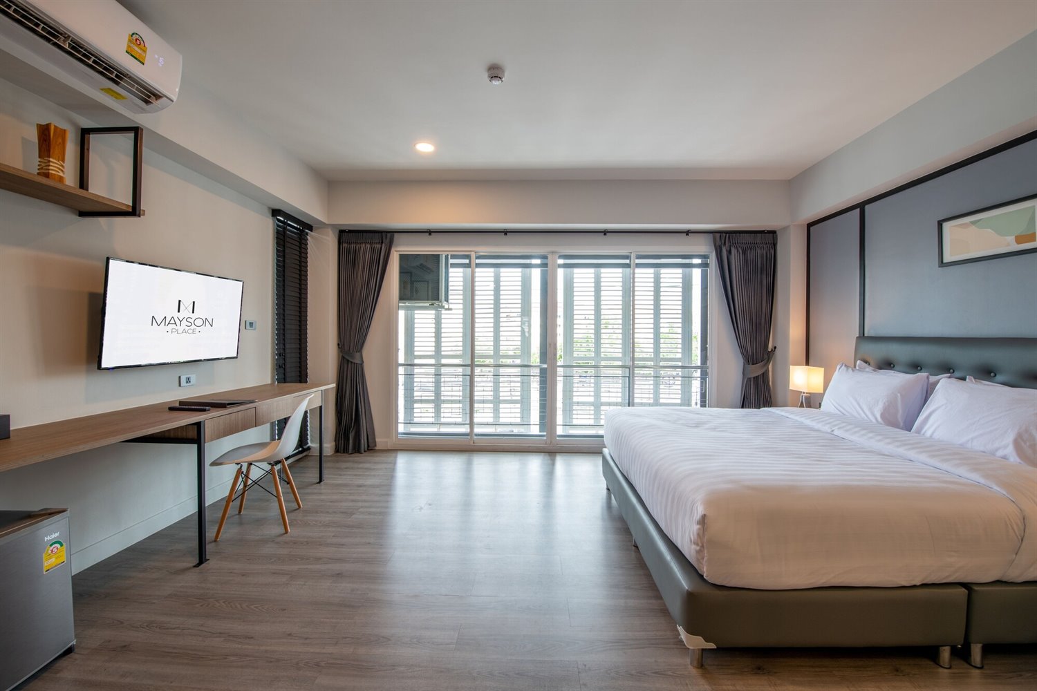 ห้อง Deluxe ของ Mayson Place โต๊ะทำงานยาว ทีวี และระเบียงกระจก