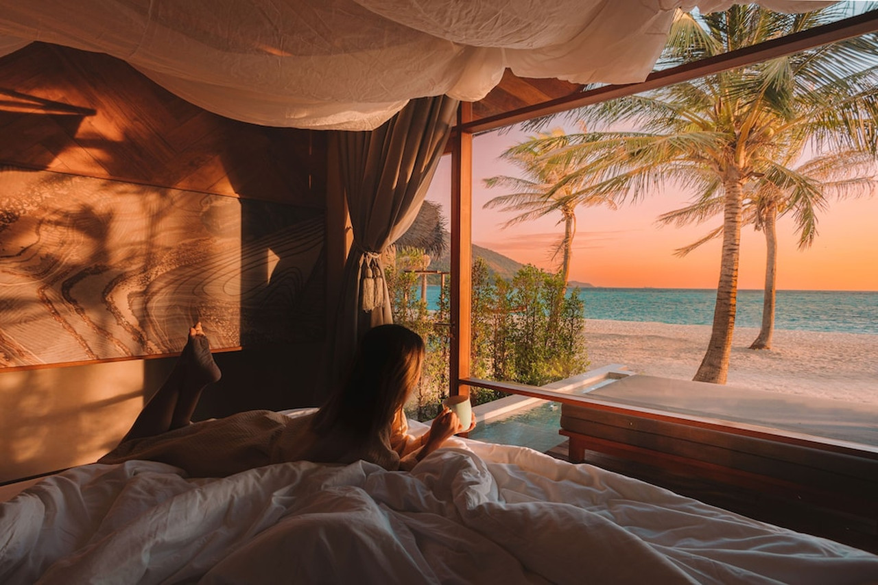 Irene Pool Villa Resort villa interior with a canopy bed and floor-to-ceiling glass overlooking the private pool and beach at sunset