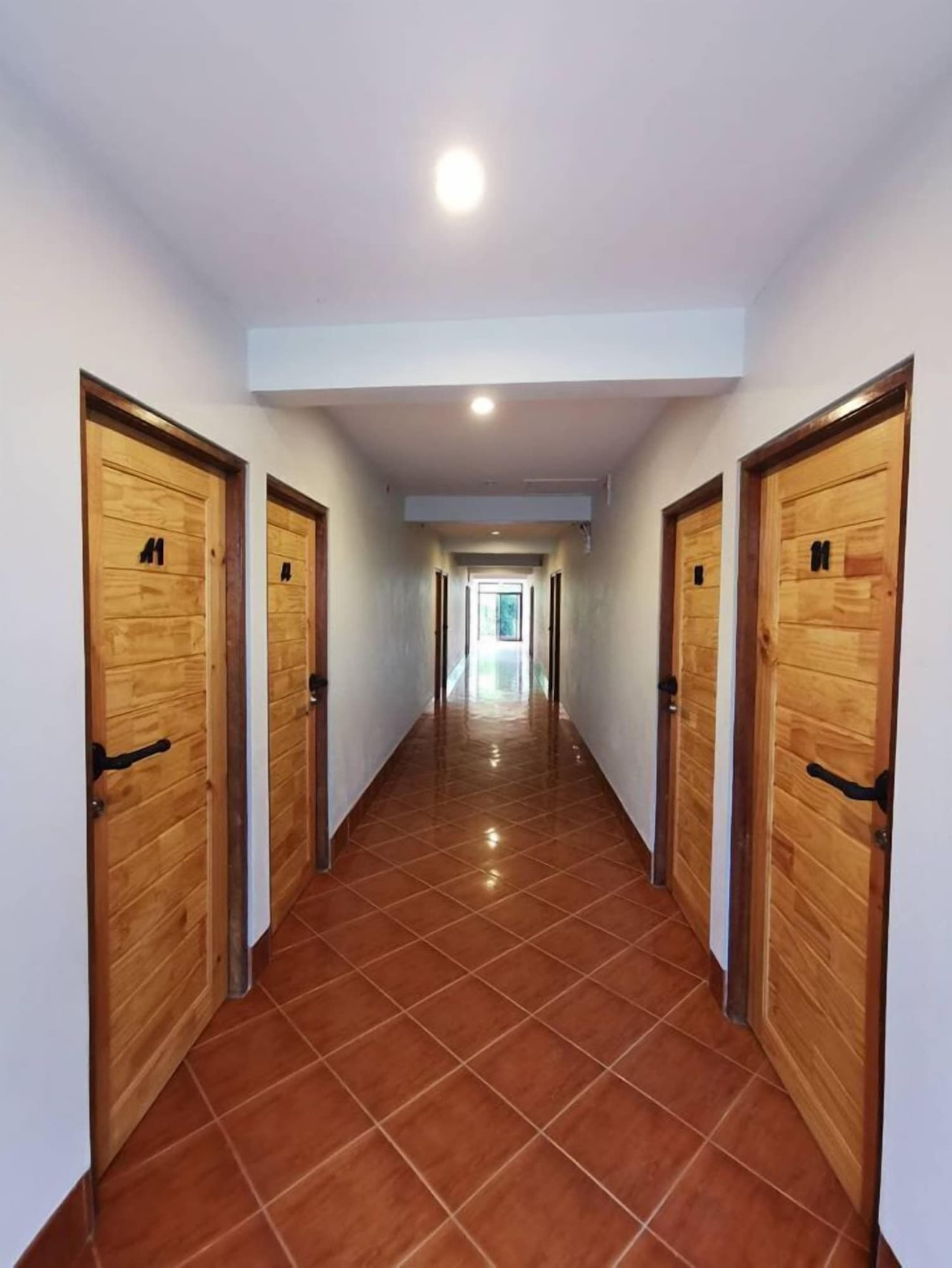 Interior corridor with wooden room doors on both sides and terracotta tiled floor