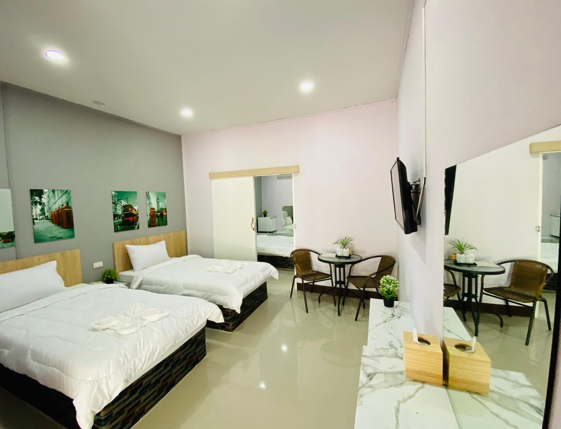 Family room in white and grey tones with twin beds, crisp white linen, a seating corner and flat-screen TV
