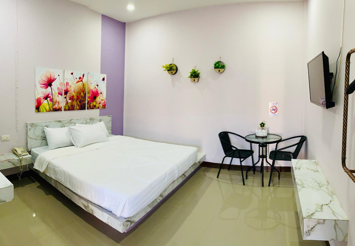 Deluxe King room with a large bed, soft purple accent wall, floral artwork, glossy floor and a table for two