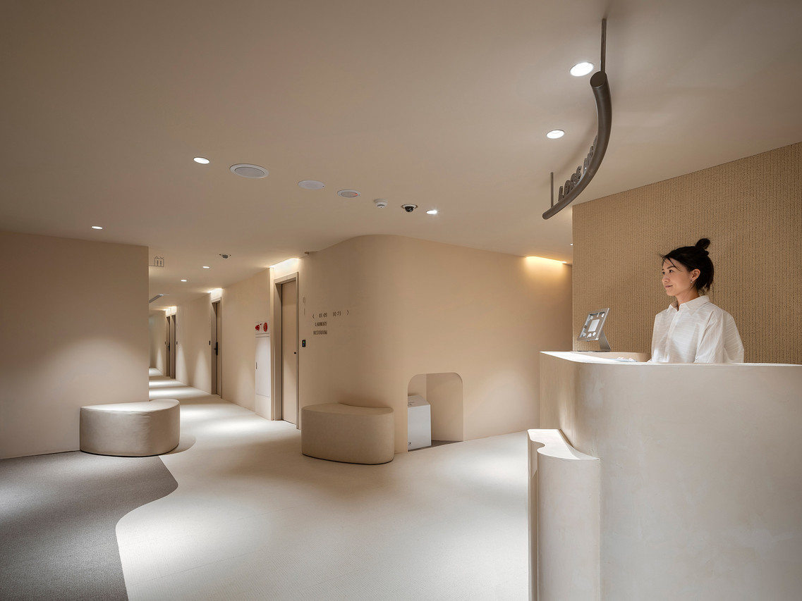 แผนกต้อนรับ Lore Hotel — เคาน์เตอร์โค้งนุ่มตัดกับทางเดินอุ่น ดีไซน์มินิมอลครีม