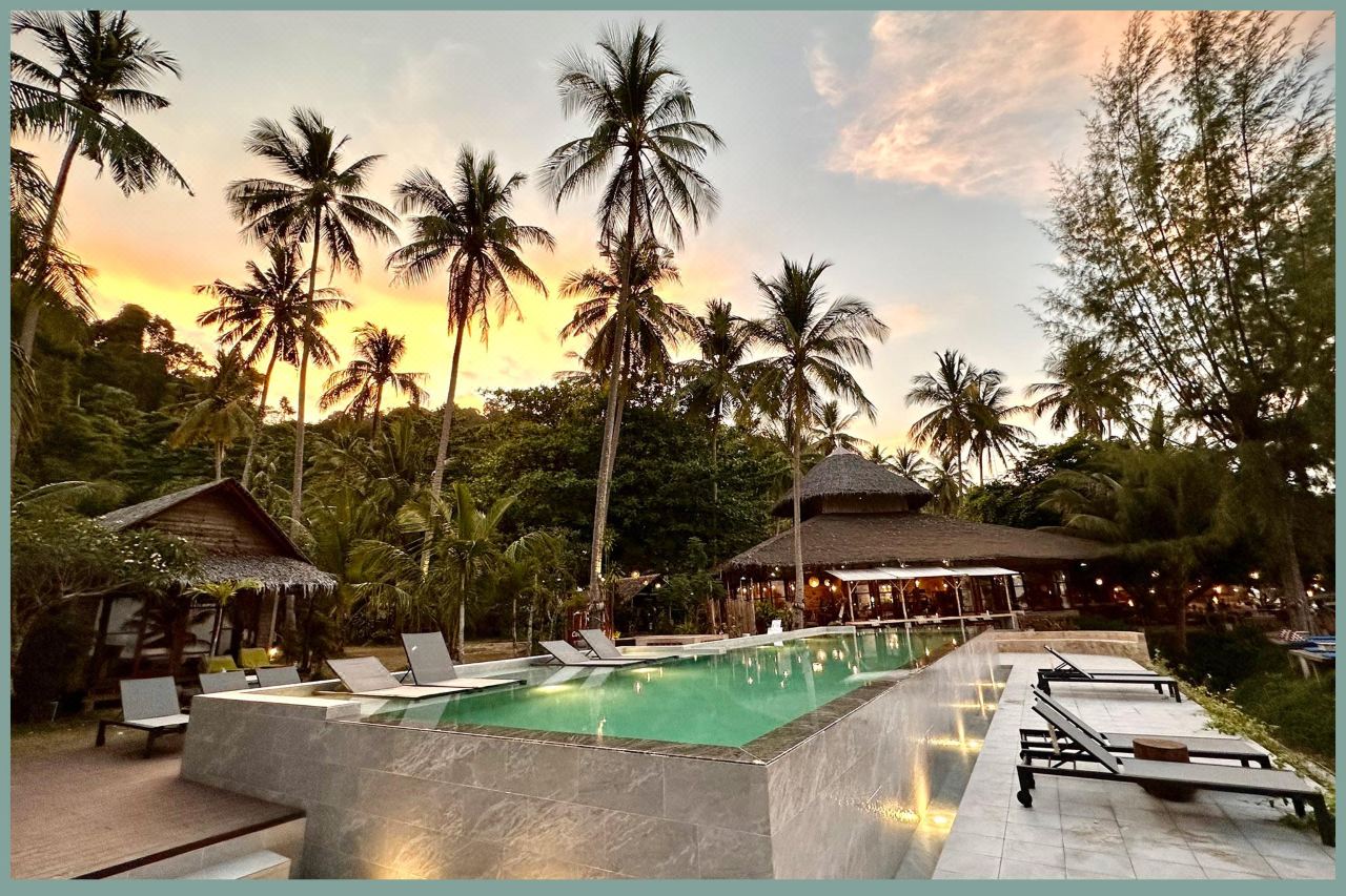 Pool and thatched-roof restaurant at sunset at Coco Cottage Koh Ngai