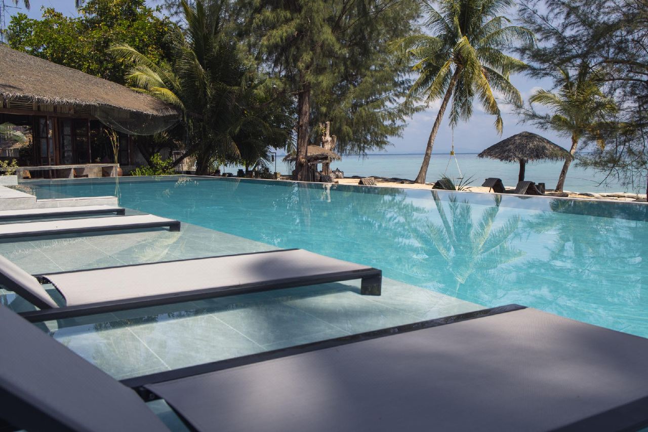 Infinity-pool edge meeting the Andaman Sea with thatched umbrellas