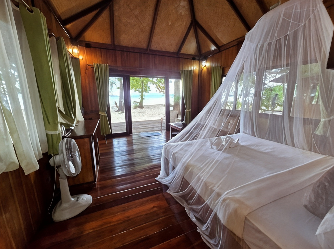 Wooden bungalow interior with mosquito net and electric fan, doors opening onto the white-sand beach at Kradan Beach Resort, Koh Kradan