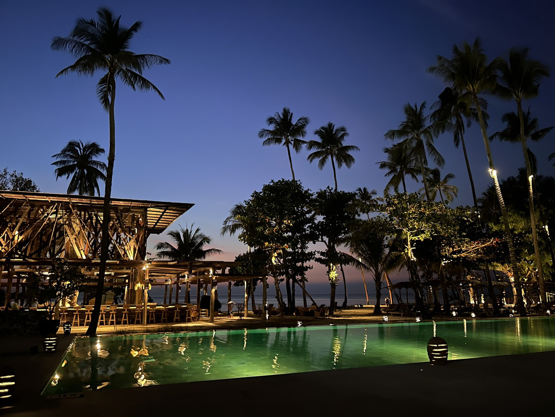 สระว่ายน้ำและบาร์ริมหาดของ The Emerald Cove Koh Chang ช่วงพลบค่ำ มีต้นมะพร้าวและทะเลด้านหลัง